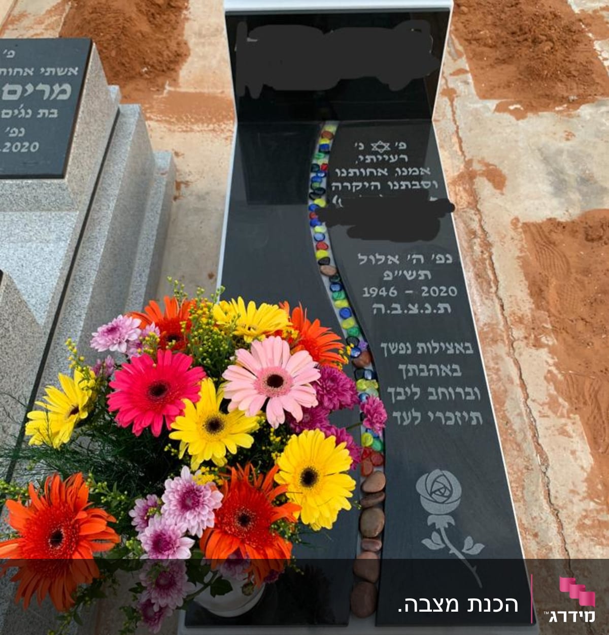 מצבה שחורה עם כיתוב בעברית ופרחים צבעוניים